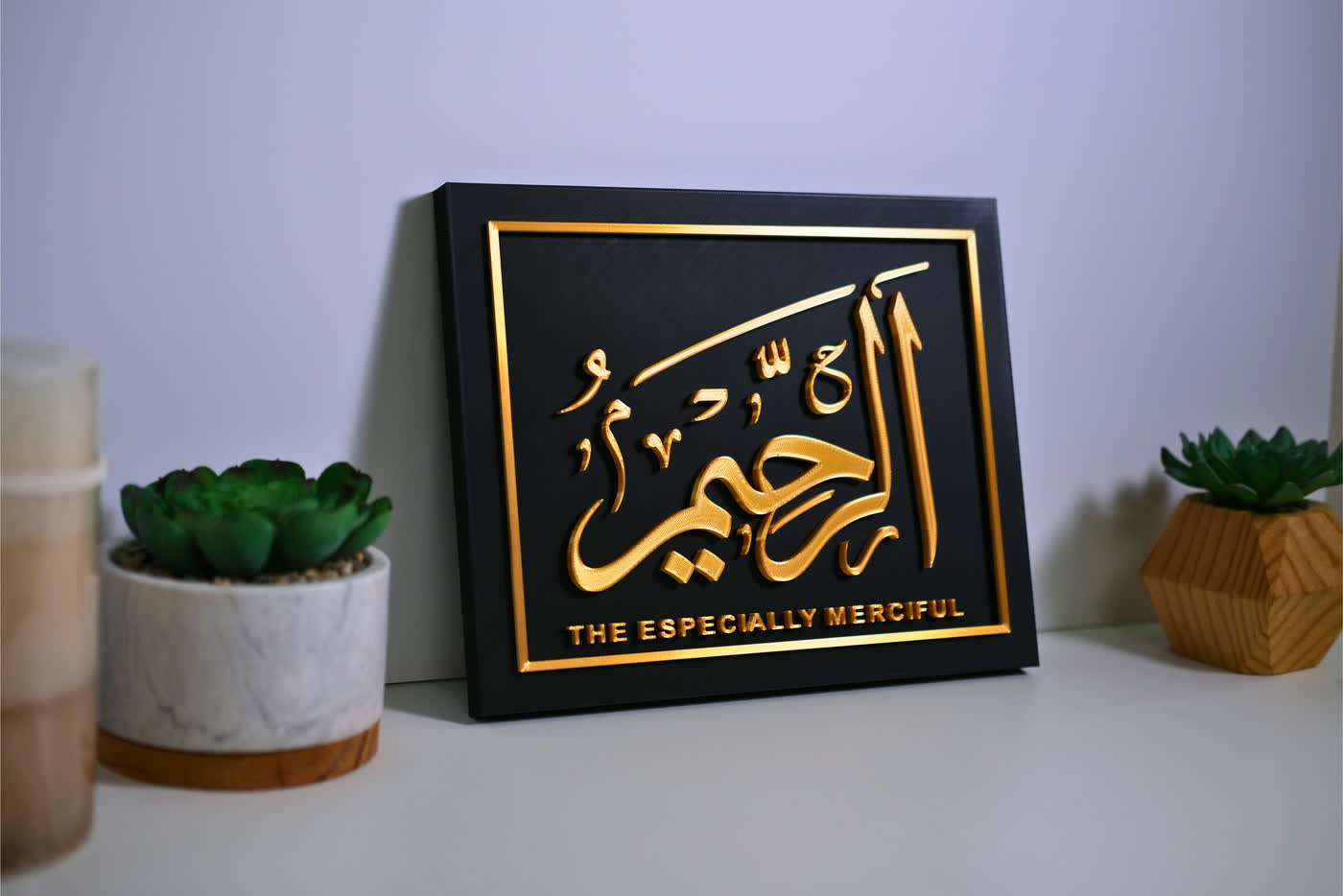 An Ar-Raheem plaque standing on a desk beside two potted plants